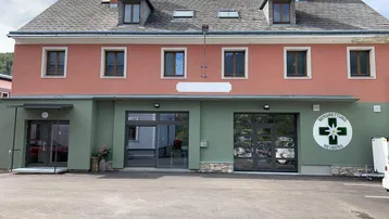Gebäude mit rosa und grüner Fassade, mehreren Fenstern und einem Satteldach mit Schornsteinen.