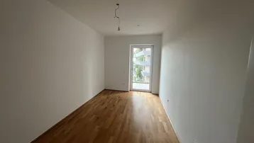 Leerer Raum mit Holzboden und Zugang zu einem französischen Balkon, hell und modern.
