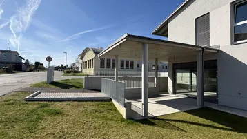 Modernes Gebäude mit überdachtem Eingangsbereich und barrierefreier Rampe unter blauem Himmel.