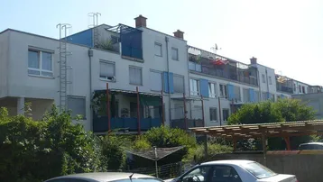 Mehrfamilienhaus mit moderner Architektur, Balkonen, Dachterrassen und Parkplätzen im Freien.
