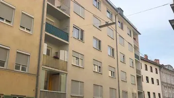 Fassade eines mehrstöckigen Wohngebäudes mit Balkonen, Rollläden und Garagen im Erdgeschoss.