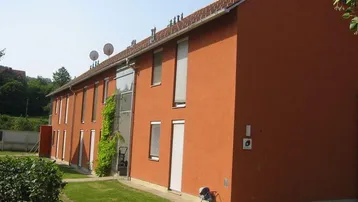 Mehrfamilienhaus mit oranger Fassade, Satteldach und grüner Umgebung an einem sonnigen Tag.
