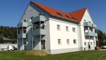 Modernes Mehrfamilienhaus mit Balkonen und Satteldach in grüner Umgebung.