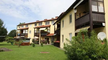 Mehrfamilienhaus mit gelber Fassade, Balkonen und einer grünen Rasenfläche im Vordergrund.