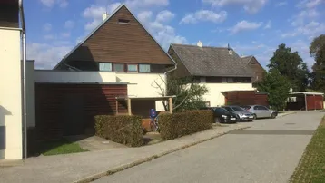 Reihenhäuser mit markanten Satteldächern und Holzfassaden, umgeben von Grünflächen und Parkplätzen.