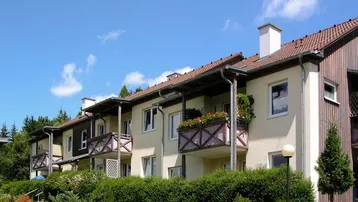 Reihenhäuser mit Balkonen und grüner Umgebung unter blauem Himmel.