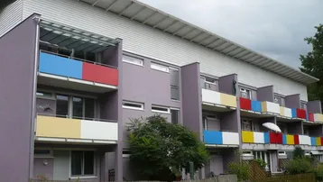 Mehrfamilienhaus mit farbenfrohen Balkonen und moderner Architektur in grüner Umgebung.