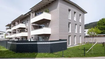 Modernes Mehrfamilienhaus mit Holzfassade, Balkonen und Blick ins Grüne, umgeben von einem gepflegten Rasen.