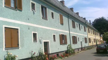 Reihenhäuser mit hellblauen und gelben Fassaden, braunen Fensterläden und Blumenbeeten entlang der Straße.
