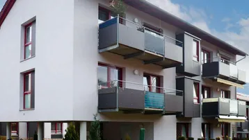 Modernes Mehrfamilienhaus mit weißer Fassade, roten Fenstern und mehreren Balkonen.