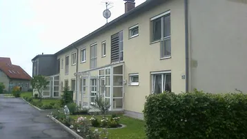 Reihenhausfassade mit hellbeigem Putz, Rollläden und gepflegtem Vorgarten.