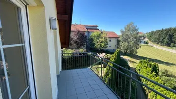 Sonniger Balkon mit Fliesenboden und Blick auf die umliegende grüne Landschaft.