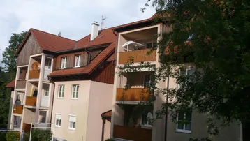 Mehrfamilienhaus mit roten Ziegeldächern, mehreren Balkonen und gepflegter Grünanlage.