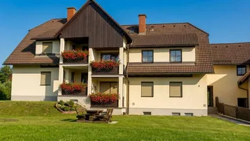 Gepflegtes Mehrfamilienhaus mit Balkonen, Blumenkästen und einem grünen Rasen im Vordergrund.