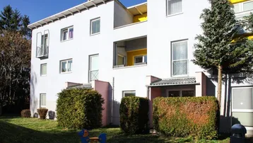Modernes Mehrfamilienhaus mit weißer Fassade, Balkonen und einem gepflegten Gartenbereich mit Spielgerät.