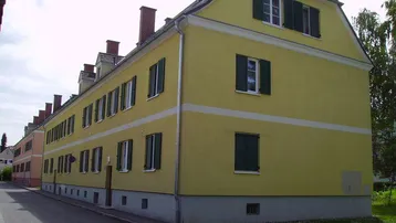 Gut erhaltenes Reihenhaus mit gelber Fassade, grünen Fensterläden und Mansarddach an einer ruhigen Straße.