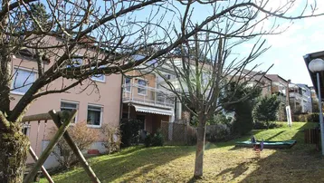 Sonniger Gartenbereich mit Spielgeräten und Blick auf die Wohngebäude mit Balkonen.