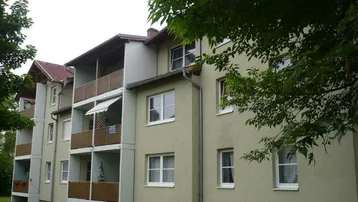 Mehrfamilienhaus mit mehreren Balkonen, umgeben von Grünflächen und Bäumen.