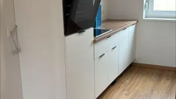 Funktionale Küche mit weißen Unterschränken, Holzarbeitsplatte und eingebautem Backofen.