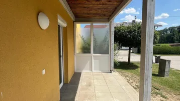 Überdachte Terrasse mit Holzbalken und Fliesenboden, angrenzend an die gelbe Hausfassade.