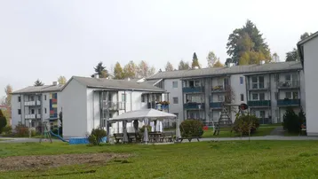 Mehrere Mehrfamilienhäuser mit Balkonen, umgeben von einer gepflegten Grünfläche und Spielplatz.