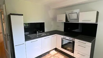 Winkelküche mit weißen Fronten, schwarzer Arbeitsplatte und integriertem Backofen und Kochfeld.