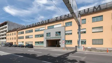 Gebäudeansicht des Technologiezentrums Linz mit Straßenfront, Einfahrt und angrenzender Baustelle.