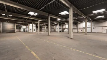 Geräumige Lagerhalle mit hoher Decke, Betonboden und Oberlichtern, ideal für industrielle Nutzung.