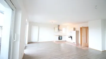 Heller, offener Wohnbereich mit integrierter Küche, modernem Bodenbelag und Zugang zum Balkon.