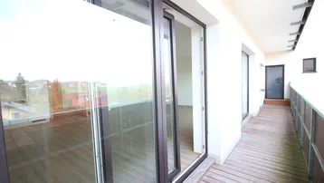 Großer Balkon mit Holzdeck und Glasgeländer, bietet weite Aussicht auf die Umgebung.