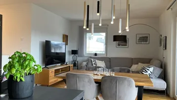 Moderner offener Wohn-Essbereich mit Holztisch, bequemer Couch und stilvoller Beleuchtung.