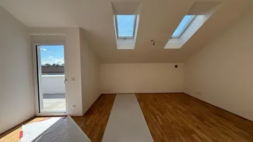 Heller Raum im Dachgeschoss mit Holzboden, Dachfenstern und Zugang zu einer Terrasse.