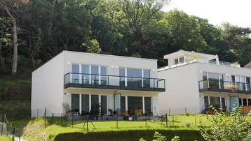 Moderne Wohngebäude mit Balkonen und Terrassen, eingebettet in eine grüne Hanglandschaft.