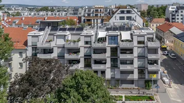 Modernes Mehrfamilienhaus mit Balkonen, Dachterrassen und Solarpaneelen auf dem Dach.