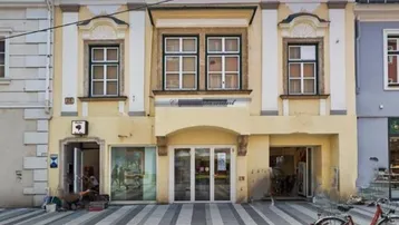Historisches Gebäude mit gelber Fassade und Geschäften im Erdgeschoss an einer belebten Straße.