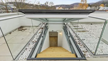 Moderner Zugang zur Dachterrasse mit Glasgeländer und weitem Blick auf die umliegende Landschaft.