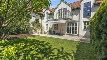 Gepflegter Gartenbereich mit Rasenfläche und einer Terrasse hinter dem Haus unter blauem Himmel.