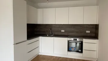 Moderne Einbauküche mit weißen Schränken, dunkler Arbeitsplatte und Holzfußboden.