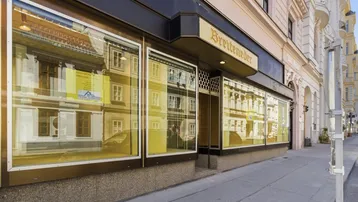 Fassade eines Geschäftsgebäudes mit großen Schaufenstern, die die gegenüberliegenden Gebäude und den Himmel widerspiegeln.