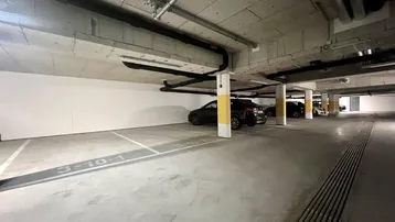 Geräumige Tiefgarage mit mehreren Stellplätzen, Betonwänden und sichtbaren Leitungen an der Decke.