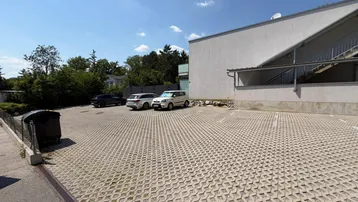 Großer Außenparkplatz mit Rasengittersteinen und modernen Gebäudefassaden im Hintergrund.