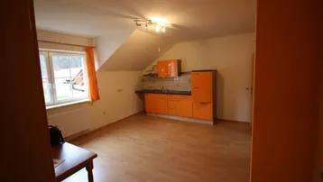 Helle Küchenzeile mit orangefarbenen Schränken, Spüle und Kühlschrank unter einer Dachschräge.
