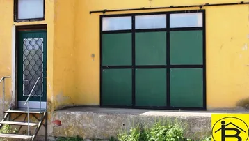Gelbe Fassade eines Gebäudes mit grüner Tür und großem Tor, das Renovierungsbedarf zeigt.