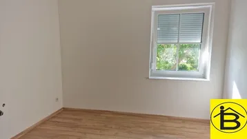 Leerer Raum mit Laminatboden und Fenster, bereit zur individuellen Gestaltung und Nutzung.