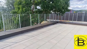 Geräumige Dachterrasse mit hellen Fliesen, Metallgeländer und Blick ins Grüne.