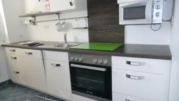 Moderne Küche mit weißen Schränken, dunkler Arbeitsplatte, integriertem Backofen und Mikrowelle.