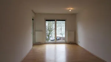 Helles Wohnzimmer mit Parkettboden und Zugang zu einem kleinen Balkon, bereit zur individuellen Gestaltung.