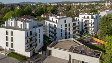 Luftaufnahme einer modernen Wohnanlage mit mehreren weißen Gebäuden, Balkonen und begrünten Außenbereichen.