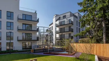 Moderne Wohngebäude mit Balkonen und einem gemeinschaftlichen Gartenbereich inklusive Spielplatz für Kinder.