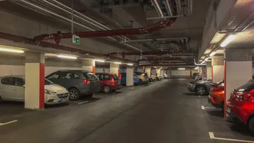 Geräumige Tiefgarage mit vielen Stellplätzen und sichtbaren Installationen an der Decke.